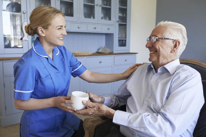 A social care worker attending to a elderly resident at a care facility with a cup of tea.