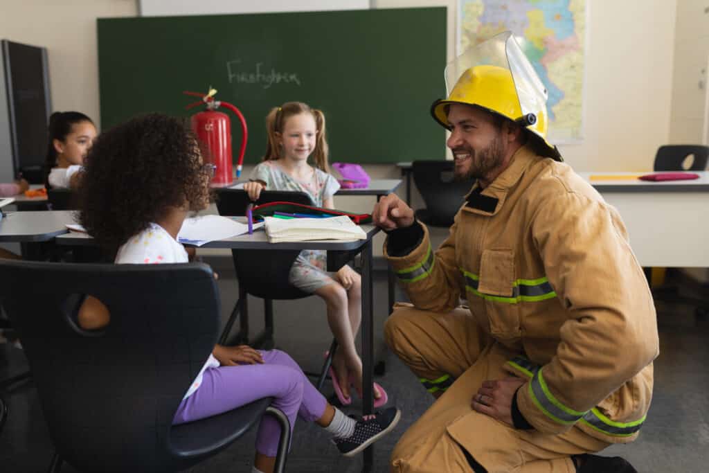 A fire fighter interacting with young students and teaching them about fire safety.